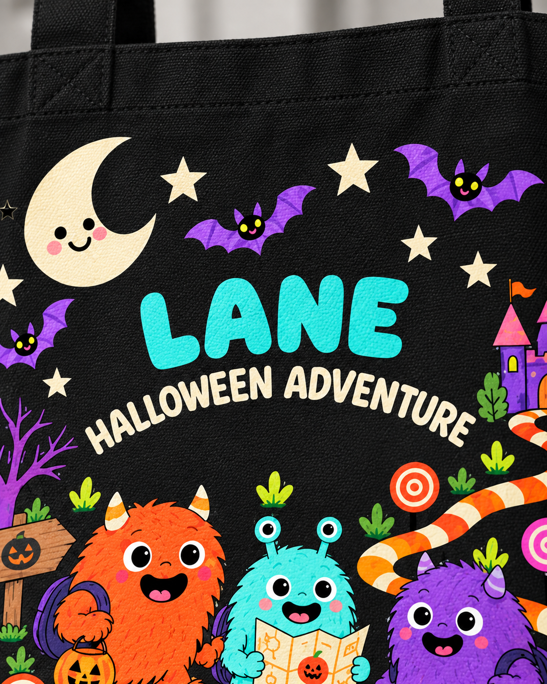 Close-up of personalized Halloween canvas tote design with the name LANE, smiling moon, castle and three colorful monsters