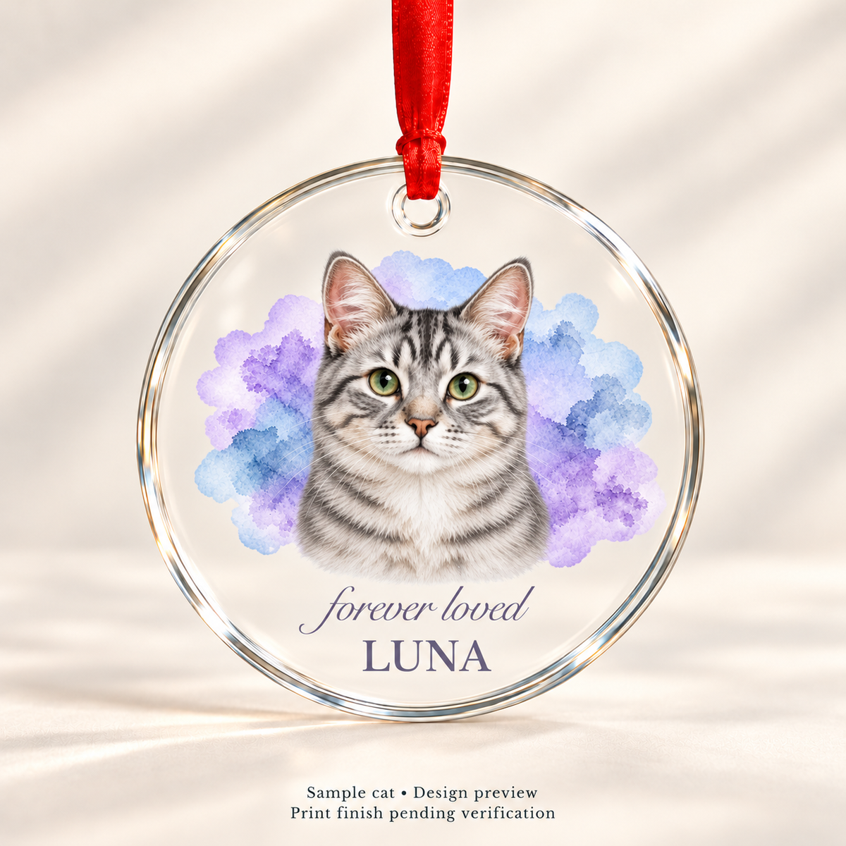 Design preview of Luna silver tabby cat memorial glass ornament with lavender-blue watercolor, forever loved script, name and red satin ribbon. Print finish pending verification.