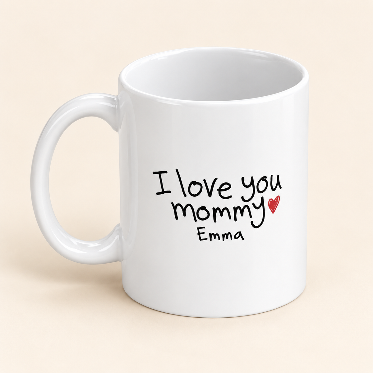 Alternate-angle view of a white ceramic mug with sample “I love you mommy” handwriting, Emma’s name, and a red heart.